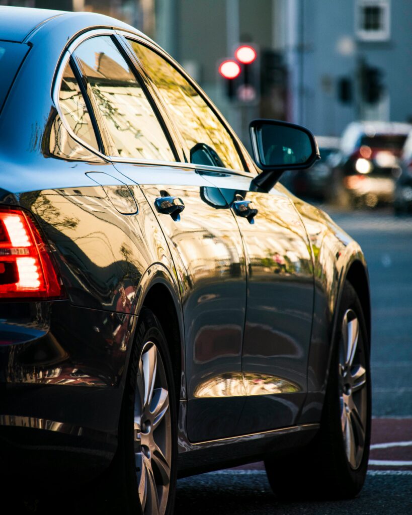 A shiny black car parked on a city street, reflecting urban surroundings.